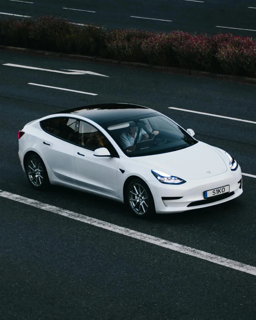 White Tesla Model 3 electric car with black roof driving on road.