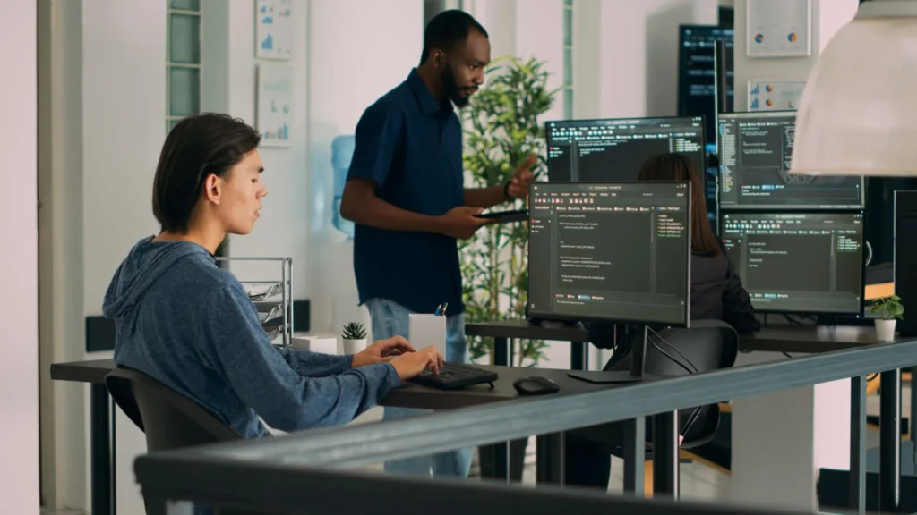 Two programmers working at computers in a modern office setting.