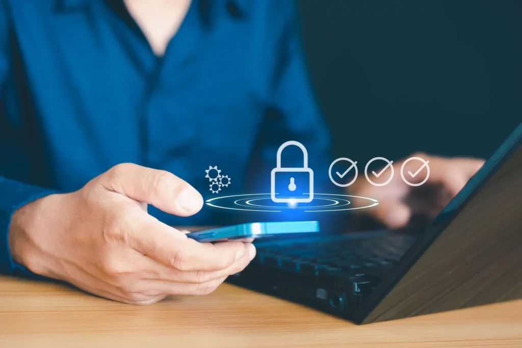 Person holding a smartphone with a laptop, featuring digital security icons.